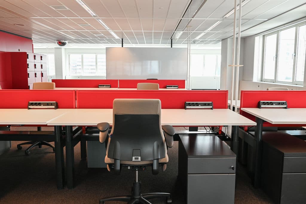 Modern office space with red dividers, white desks, gray chairs, and large windows. Bright, organized, and ready for work.