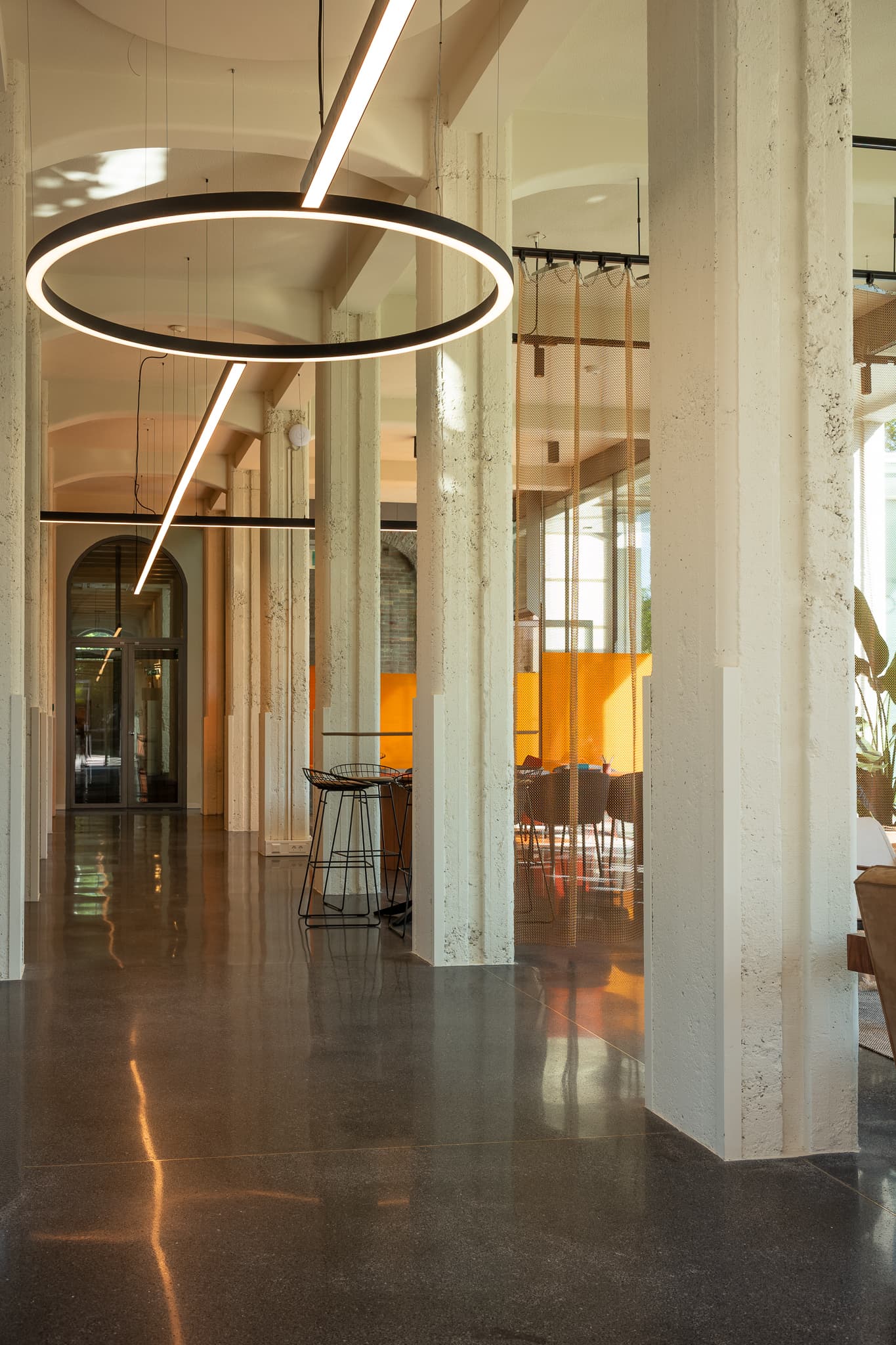 Modern building entrance with glass facade, revolving door, and people walking. Interior features stairs, plants, and framed pictures.