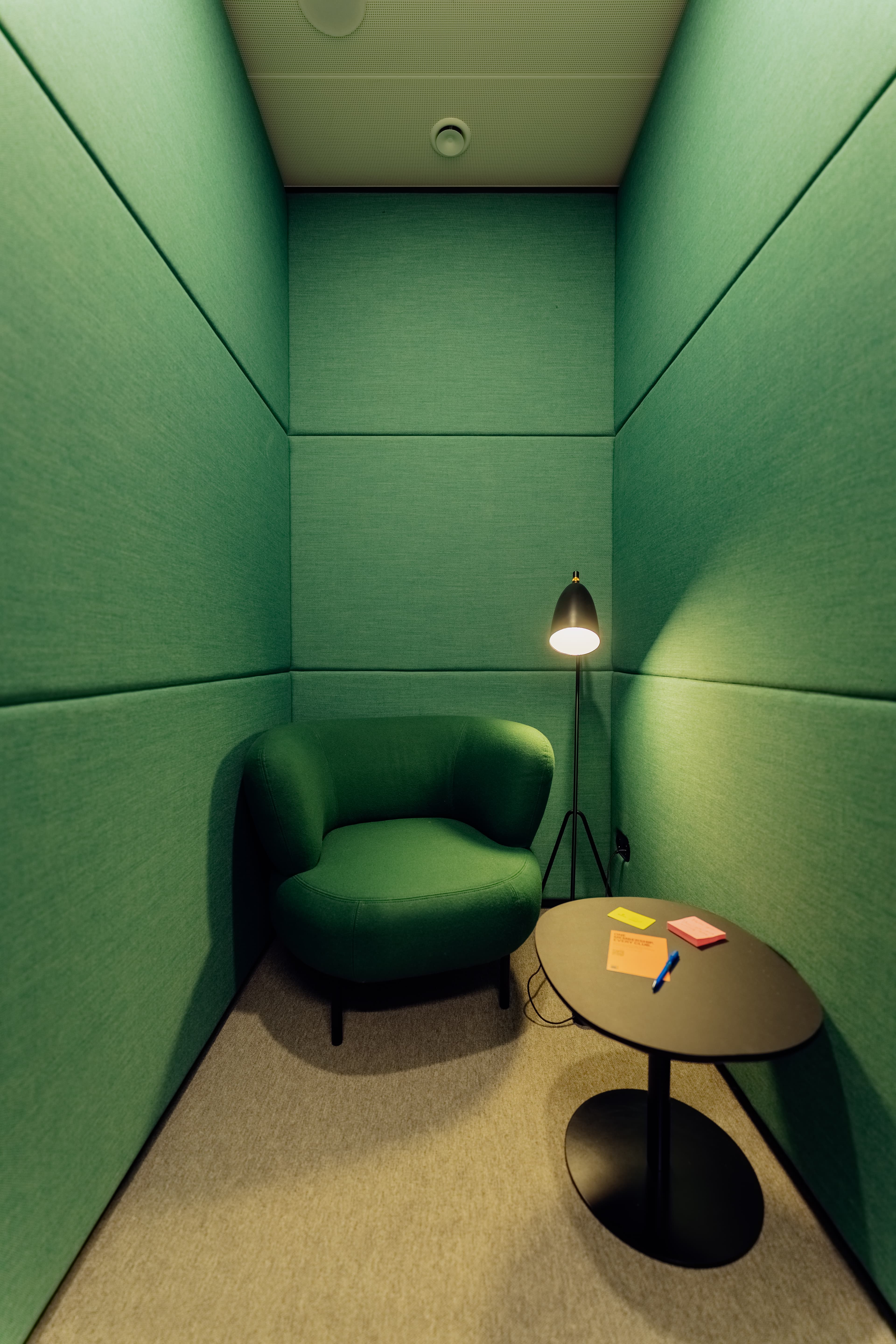 Cozy green room with an armchair, black floor lamp, and small table holding notepads and a pen.