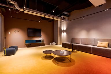 Modern office lounge with glass walls, featuring cozy seating, round tables, and warm lighting. A minimalist design with a neutral color palette.