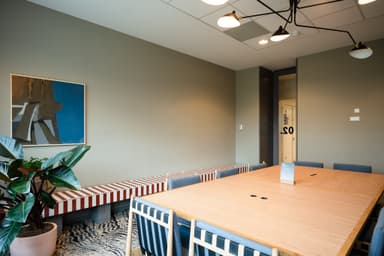Modern meeting room with a wooden table, blue chairs, a striped bench, a painting on the wall, and a potted plant.