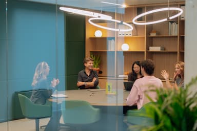 A group of people having a meeting in a modern office with bookshelves, indoor plants, and circular ceiling lights.