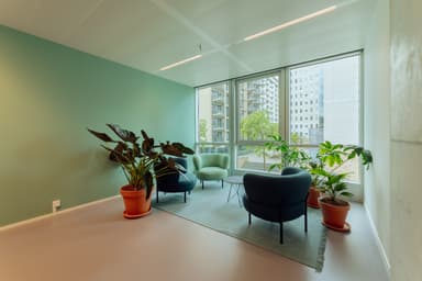 Minimalist sitting area with modern chairs, large windows, and potted plants, featuring a teal accent wall and city views outside.